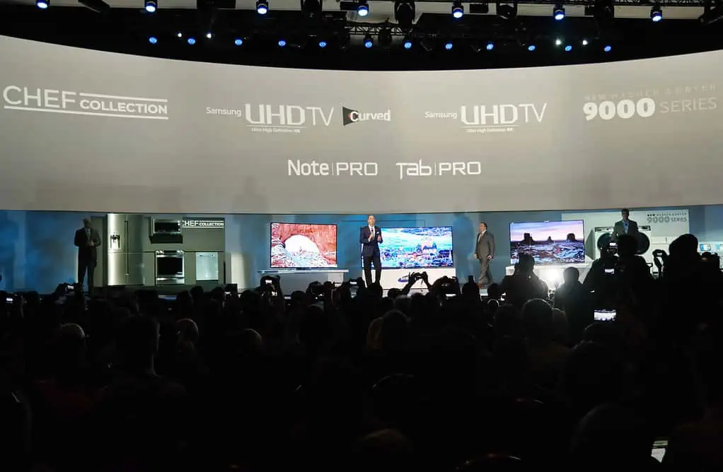 A chef is demonstrating the features of a Samsung UHDTV Curved UHDTV 9000 Series and a NotePRO TabIPRO 900045. Full Text: CHEF COLLECTION Sansung UHDTV Curved UHDTV 9000 SERIES Note|PRO TabIPRO 900045